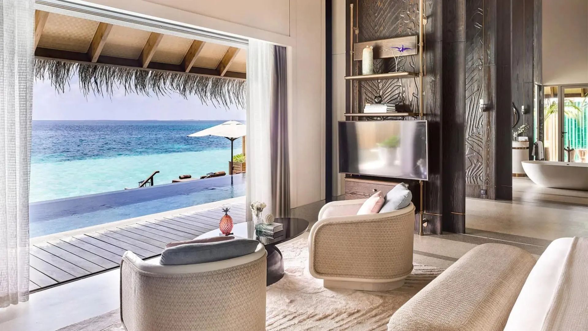 Blick aus dem Wohnbereich einer Villa durch die geöffnete Terrassentür auf den Pool und das Meer.