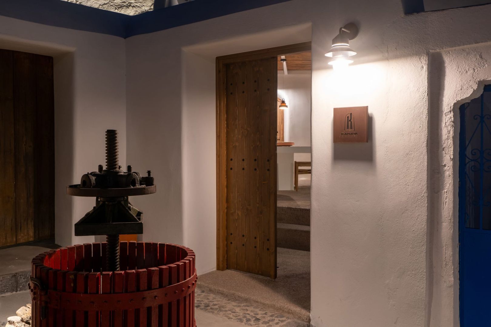 Historische Weinpresse aus Holz vor einer hellen Wand und Holzschiebetür.