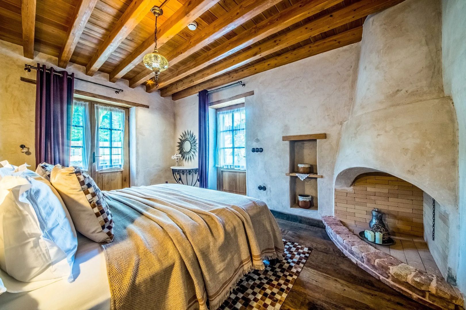 Helles Schlafzimmer mit Kamin, Holzbalkendecke und Fensterfront.