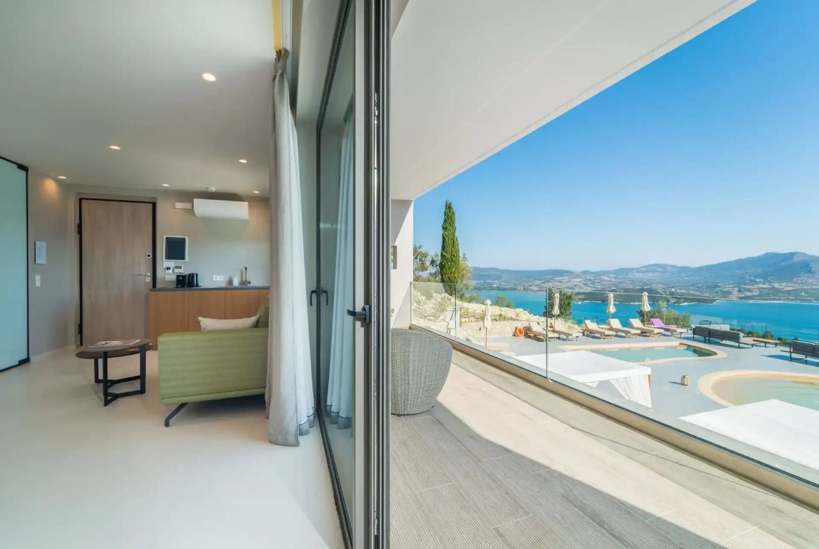 Blick von der Suite über den Balkon auf die umliegende Landschaft, den Poolbereich und das Meer.