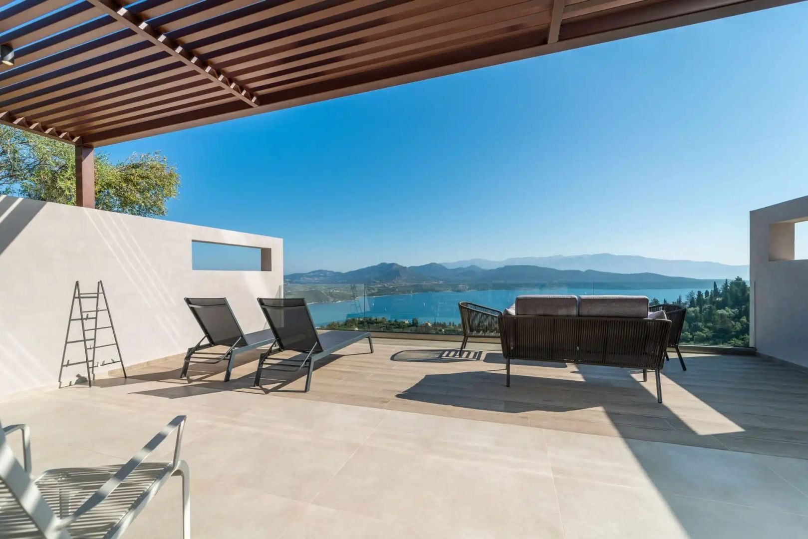 Sonnige Terrasse mit Sonnenliegen, Outdoor-Sofa und Weitblick auf Meer und Berge.