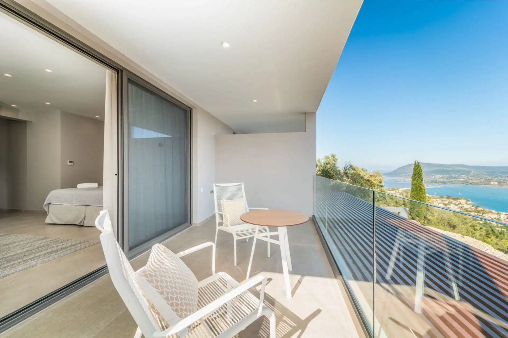 Überdachter Balkon mit zwei weißen Stühlen, einem Tisch und einem Glasgeländer.