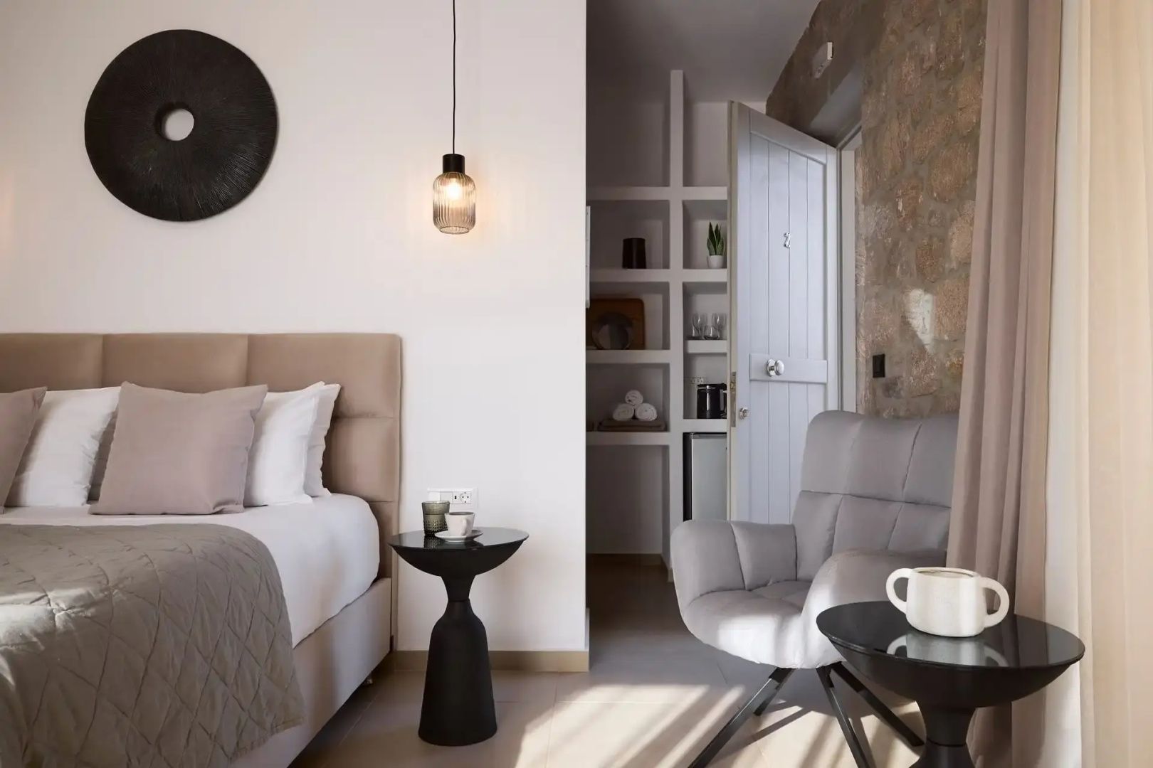 Suiten Einrichtung mit Bett, Beistelltisch, Sessel und offenen Regalen im Hintergrund.