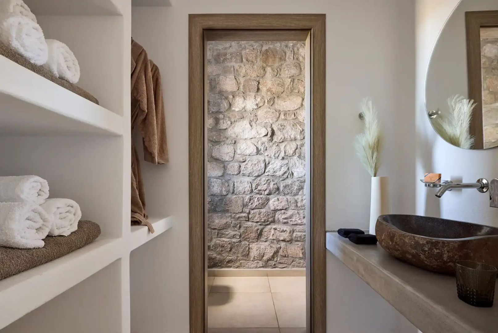 Blick durch eine Holztür auf ein Badezimmer mit Natursteinwand und Waschtisch.