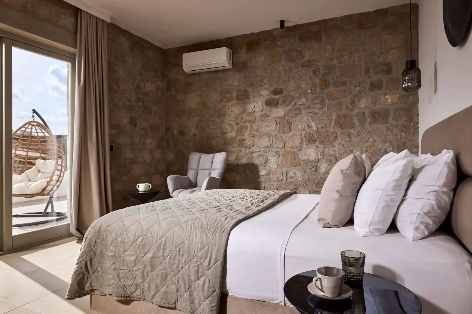 Schlafzimmer mit Natursteinwand, Doppelbett, Klimaanlage und einem Sessel in der Ecke.