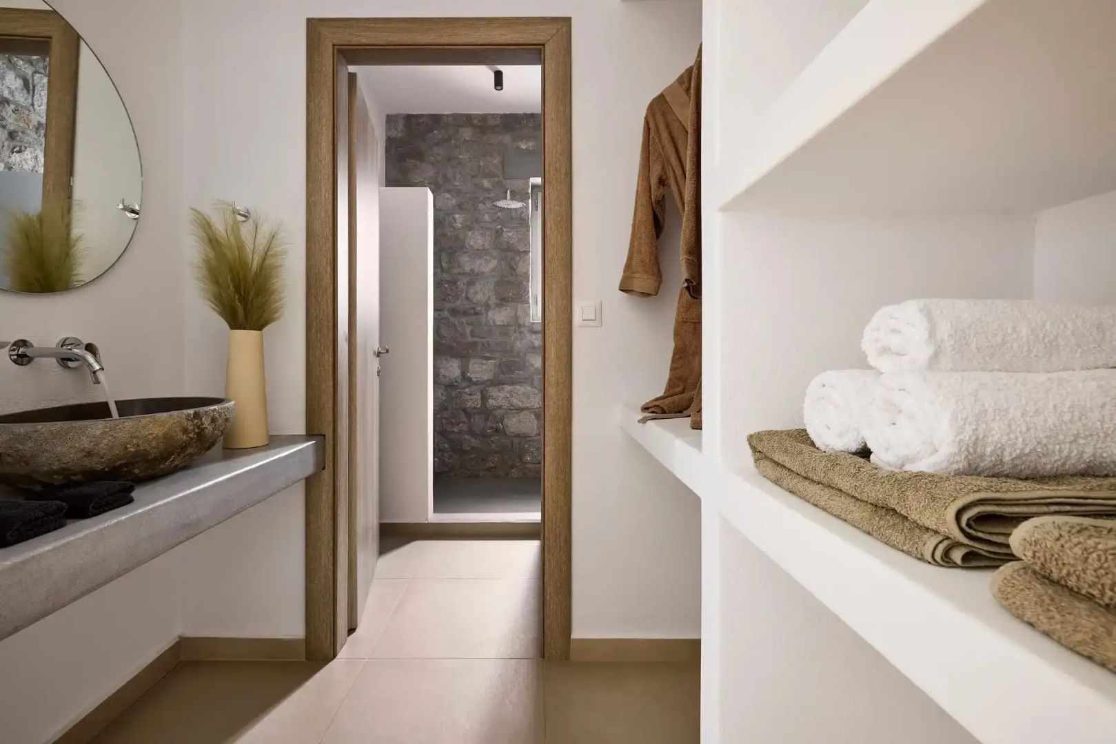 Badezimmerbereich mit Ablageregal, Handtüchern, Bademantel und Durchgang zur Dusche.