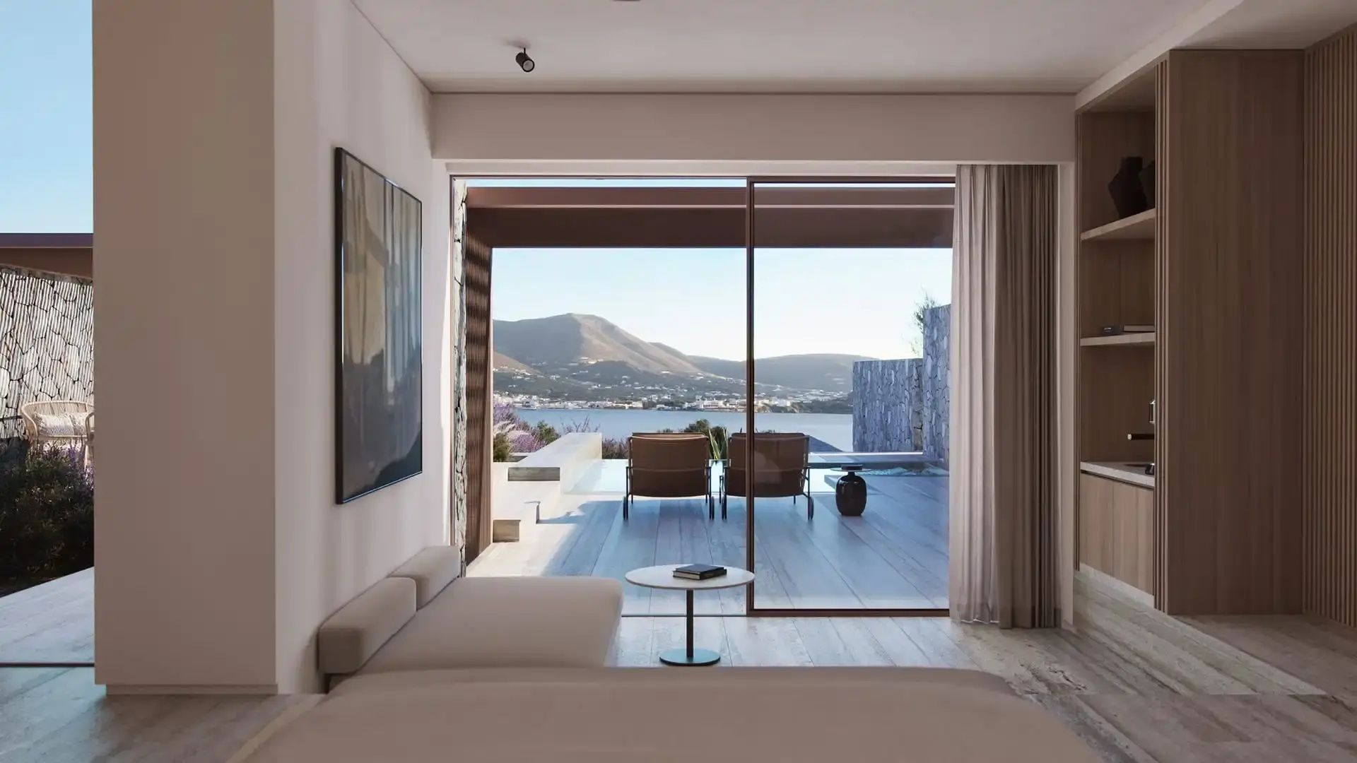 Blick vom Zimmer durch große Glasfront auf Terrasse mit Sonnenliegen, Pool und Meer.