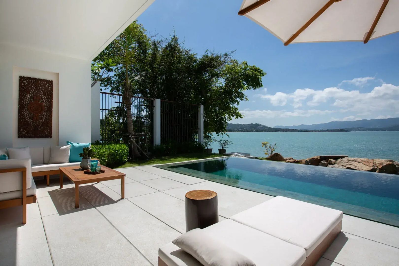 Sonnenterrasse mit privatem Pool, Sonnenliege und Blick auf das Meer unter blauem Himmel.