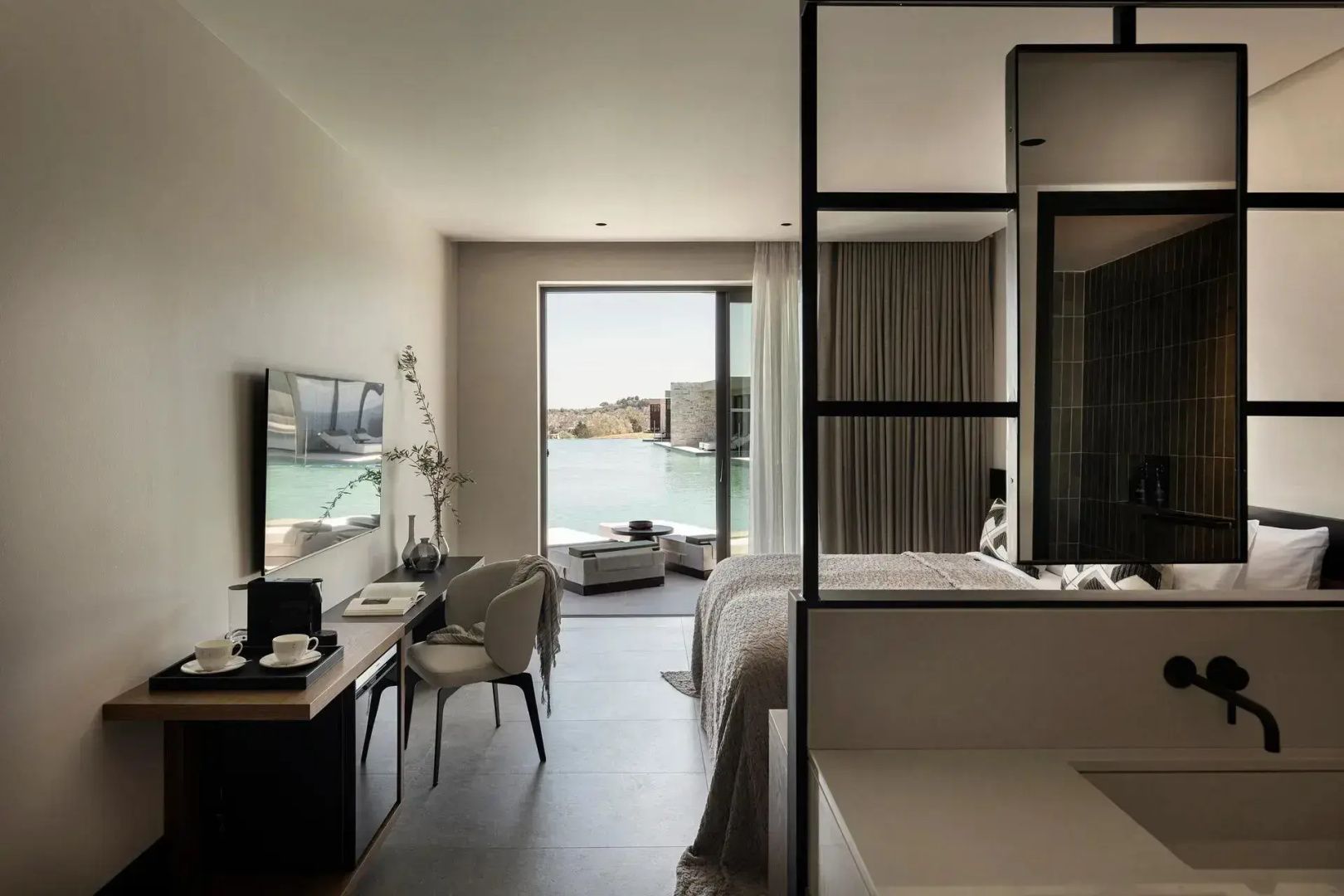 Modernes Hotelzimmer mit Doppelbett, Schreibtisch und Blick auf die Terrasse mit Pool.