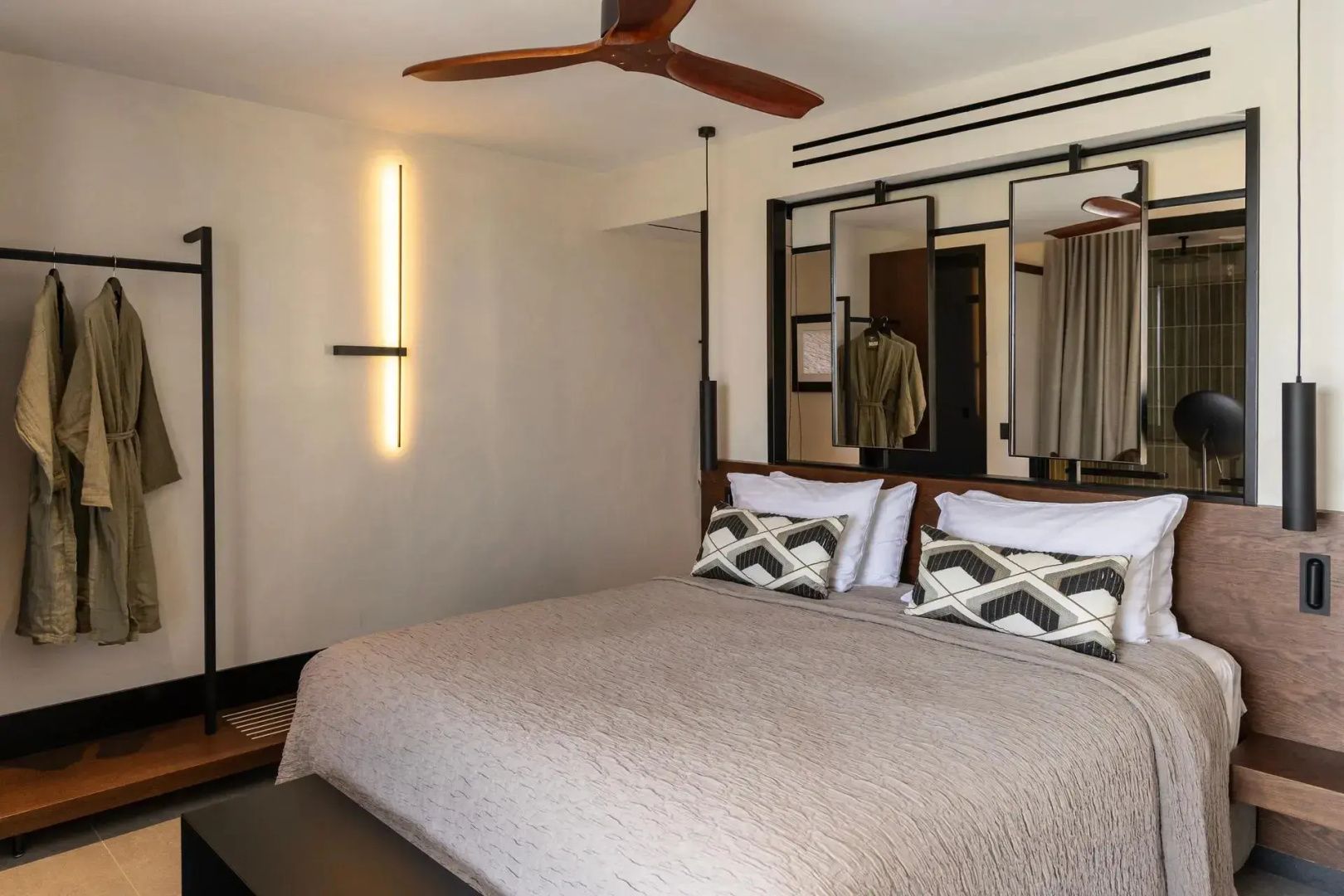 Doppelbett mit gemusterten Kissen, Holzventilator an der Decke und einer modernen Wandleuchte.