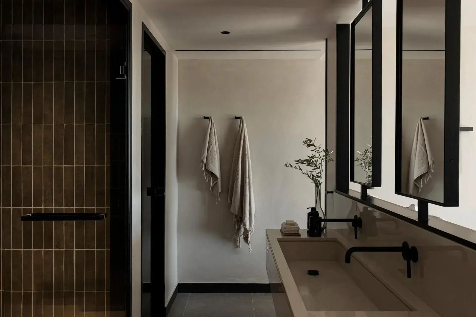 Badezimmer mit Waschtisch, Spiegel, Armaturen und an der Wand hängenden Handtüchern.