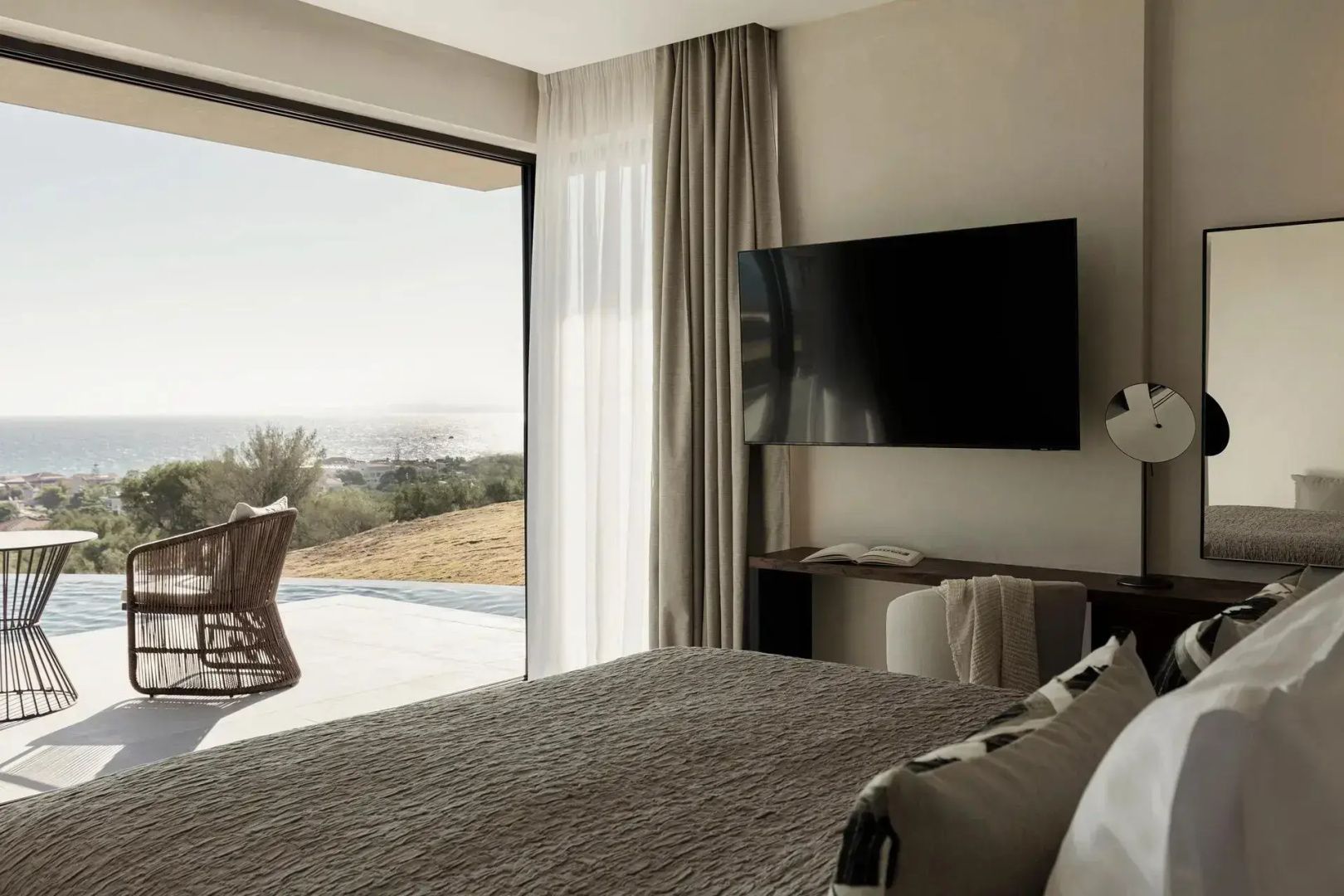 Hotelzimmer mit Blick durch die geöffnete Terrassentür auf die Landschaft und das Meer.