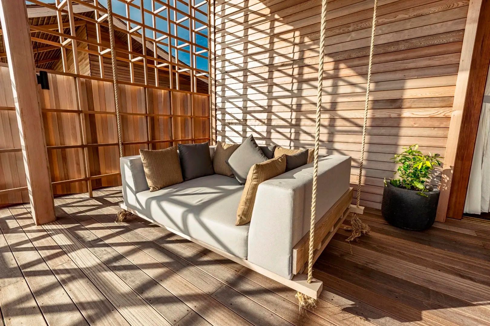 Hängendes Loungesofa aus Holz auf einer schattigen Holzterrasse.