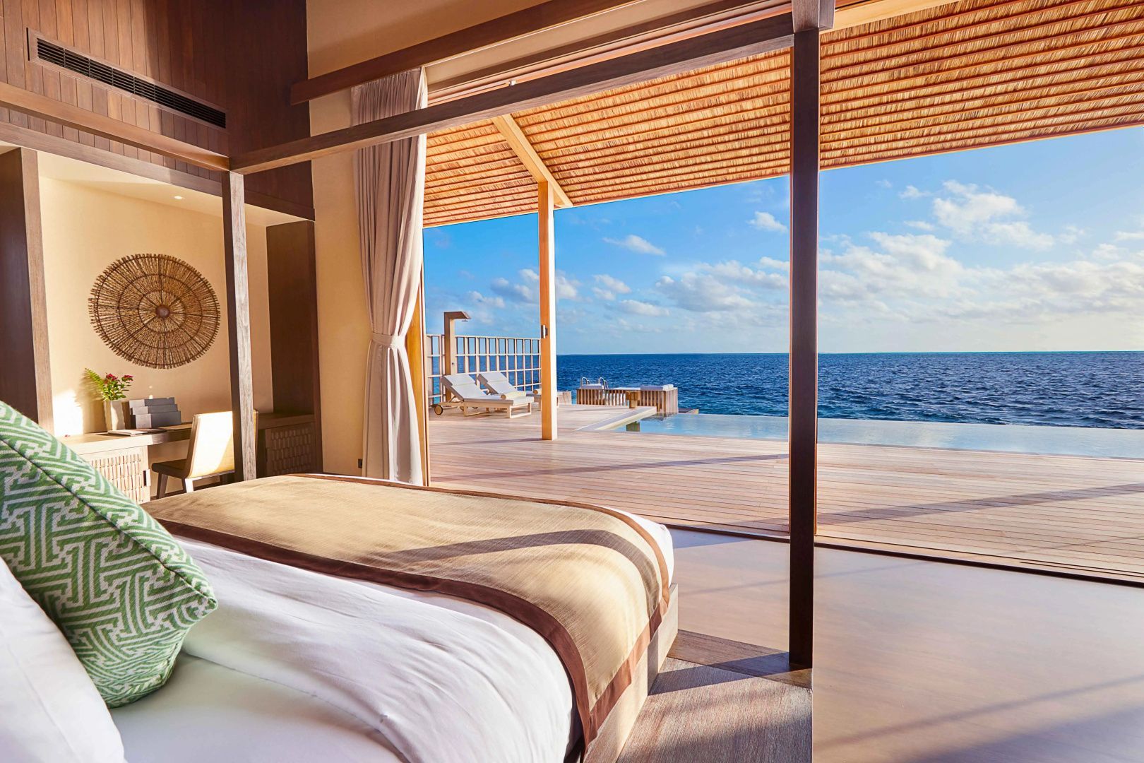 Blick aus einem Schlafzimmer über eine Holzterrasse mit Pool direkt auf das offene Meer.