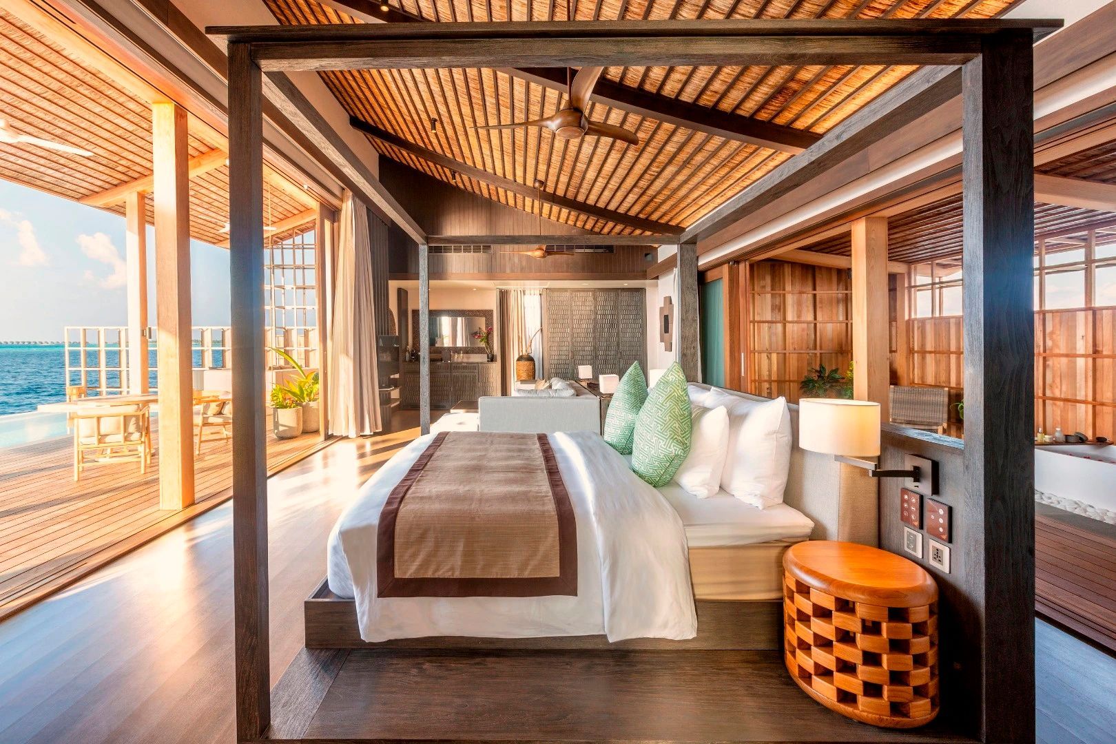 Schlafbereich einer Overwater Villa mit großem Himmelbett und Holzdecke.