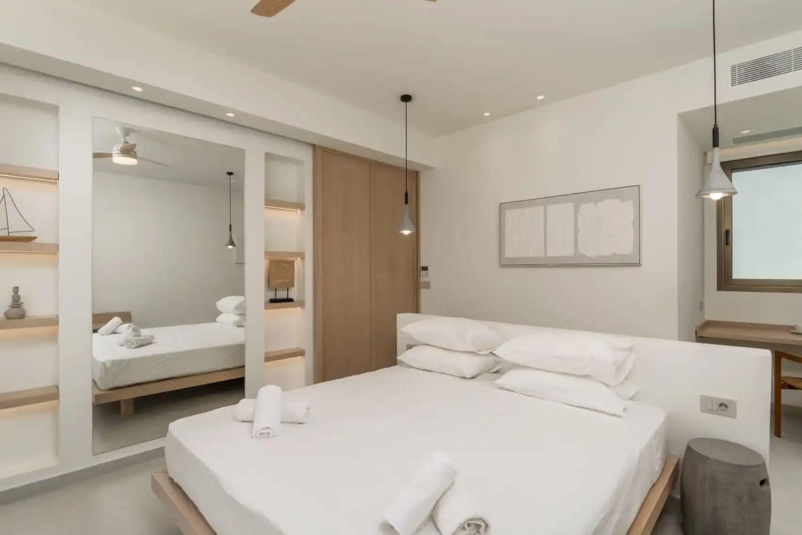 Hell eingerichtetes Schlafzimmer mit Doppelbett, weißen Handtüchern, Holzschrank und großem Spiegel.