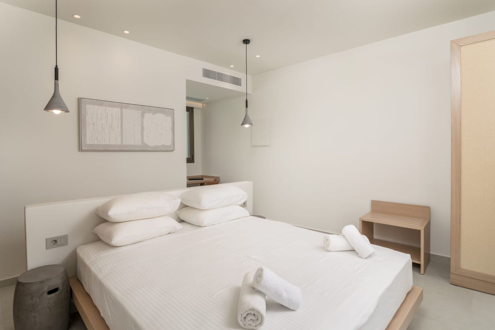 Minimalistisches Schlafzimmer mit weiß bezogenem Doppelbett, aufgerollten Handtüchern und heller Wand.