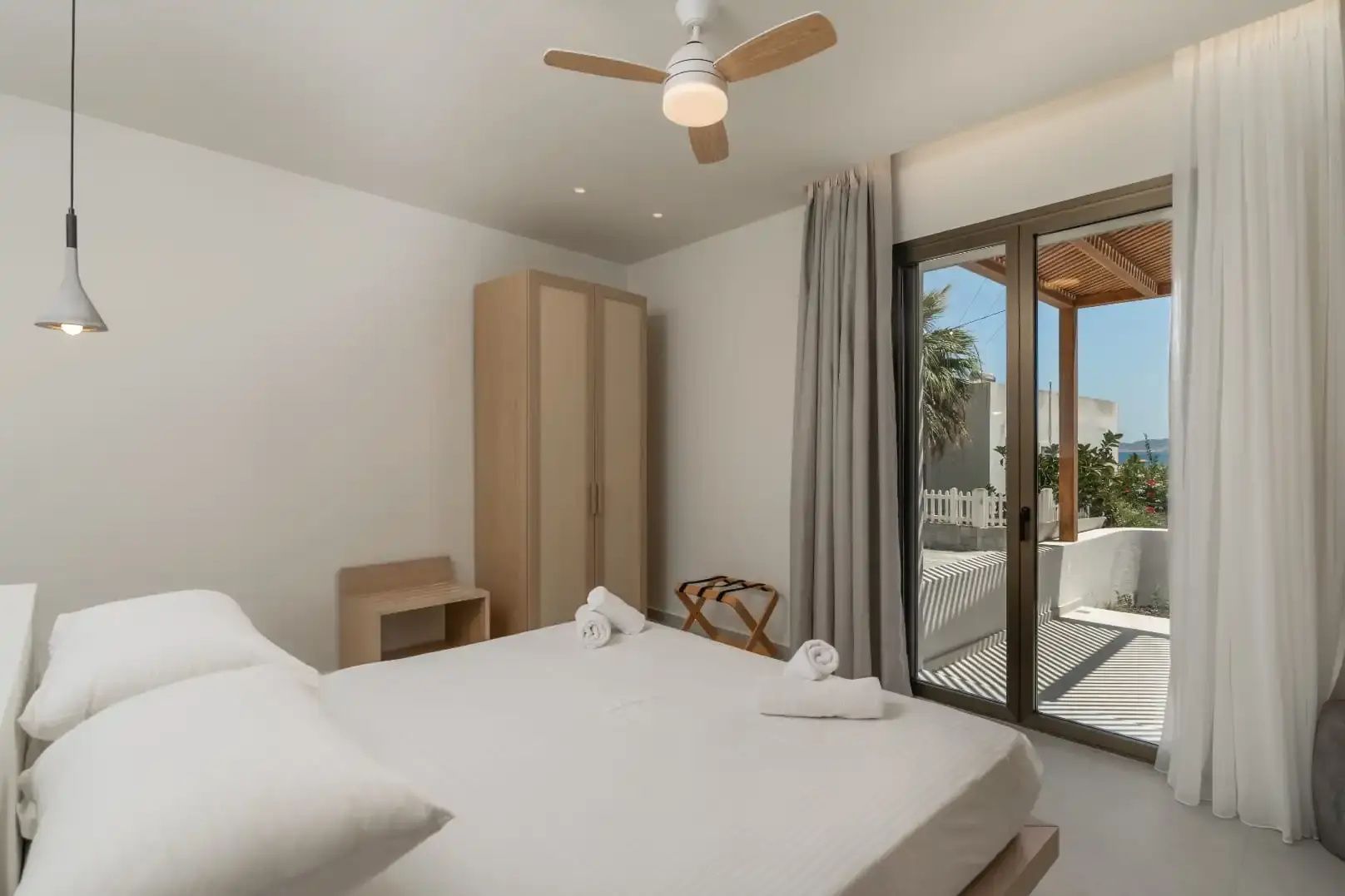 Schlafzimmer mit hellen Holzmöbeln, Deckenventilator und Schiebetür zur sonnigen Terrasse.