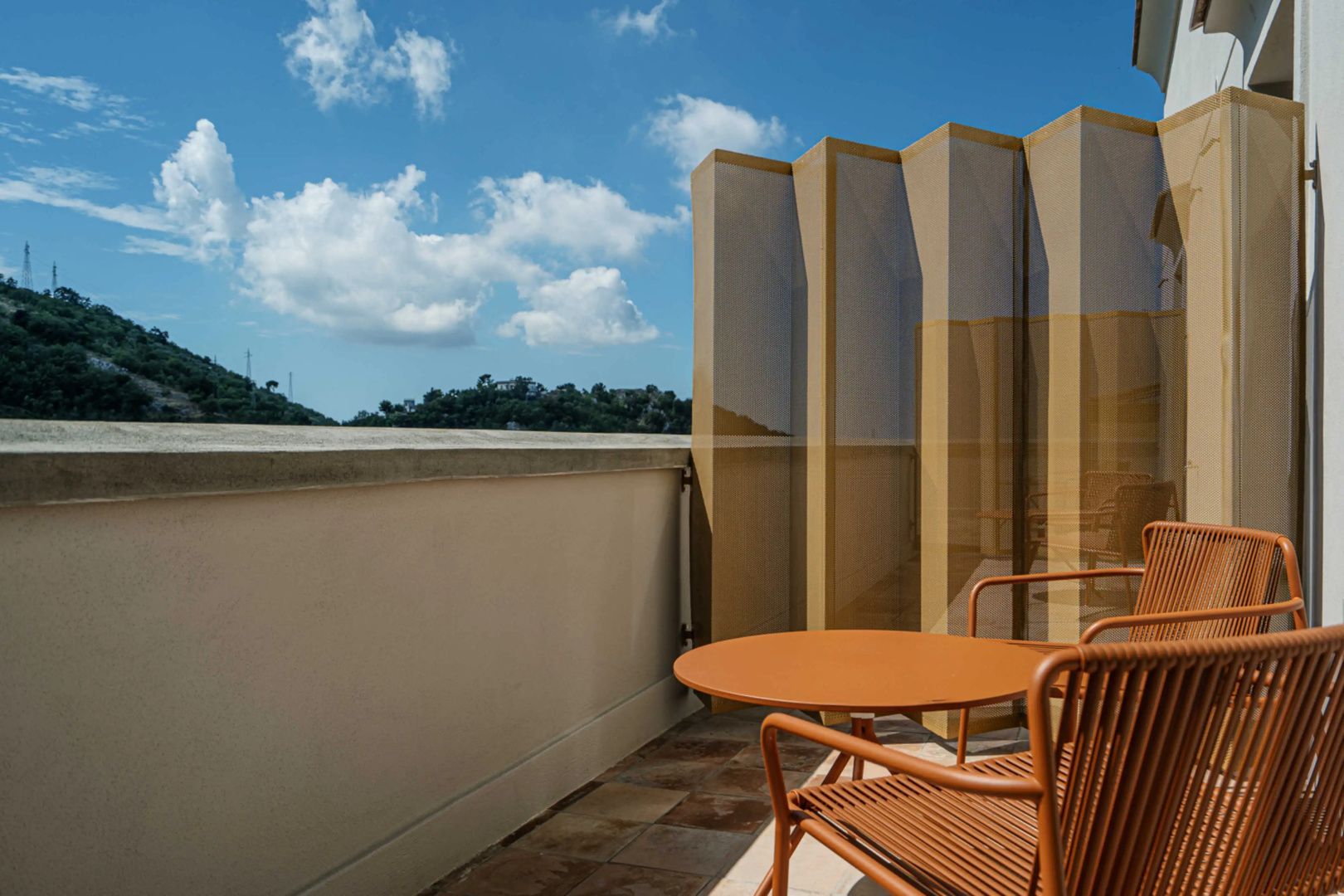 Terrassenbereich mit orangefarbenem Tisch, Stuhl und Blick auf umliegende Hügel.