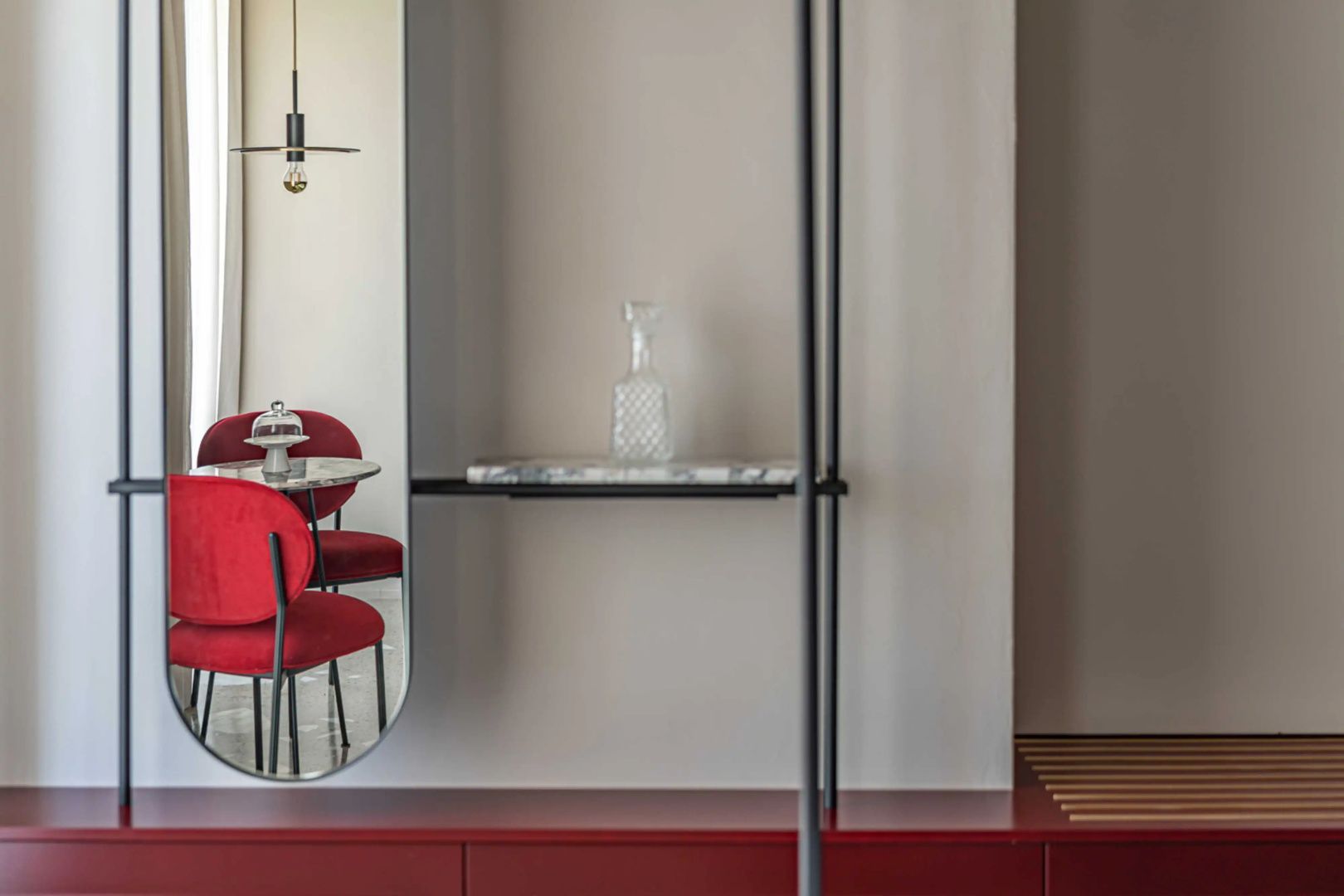 Rotes Sideboard mit Glaskaraffe und großer Spiegel, der rote Stühle im Raum widerspiegelt.
