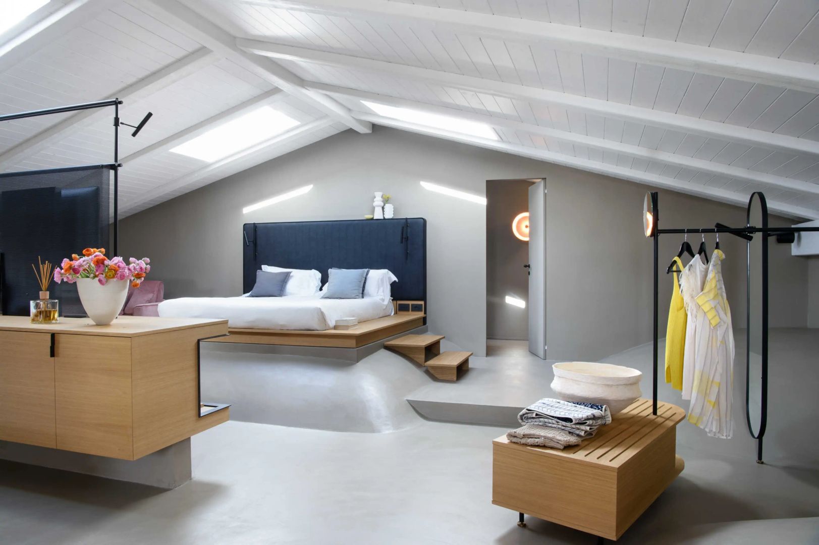 Dachgeschoss-Schlafzimmer mit Doppelbett auf einem Sockel und weißen Holzbalken.