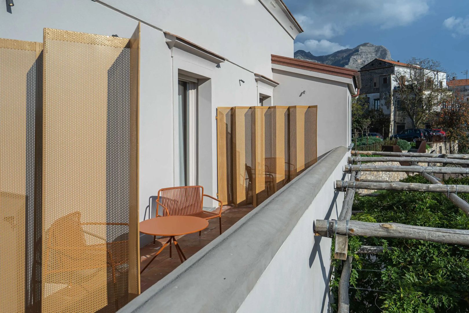 Balkon mit orangen Metallstühlen, Tisch und gelbem Sichtschutz vor weißer Fassade.