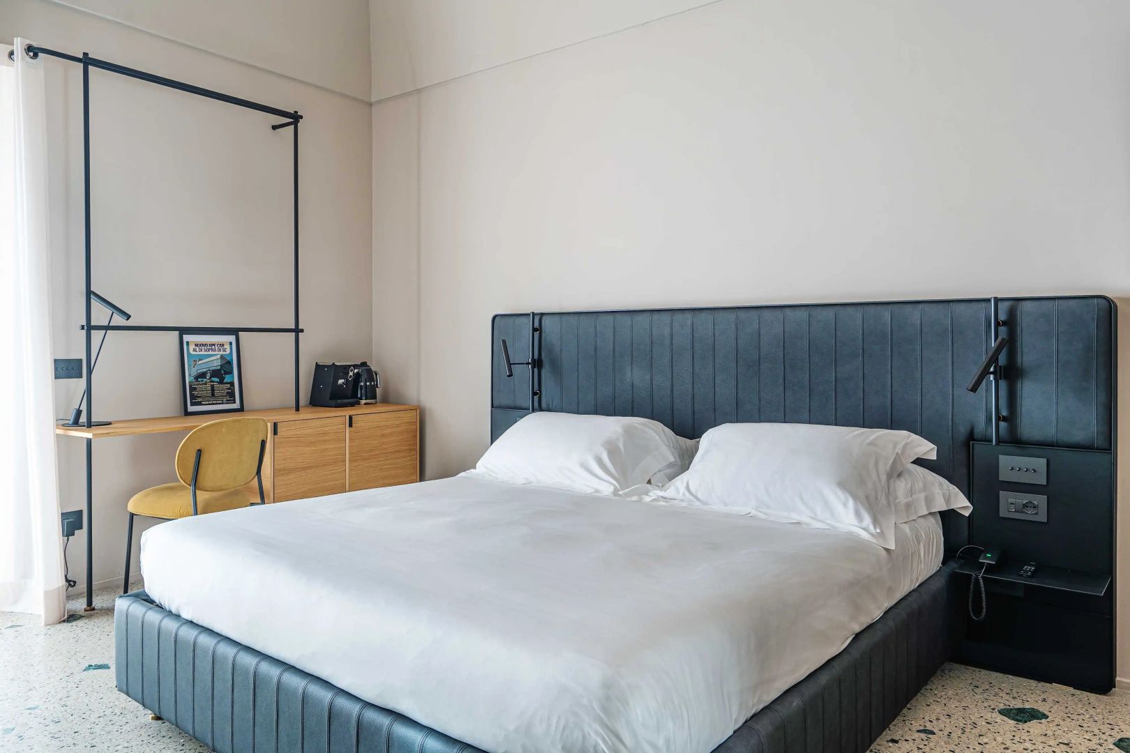 Doppelbett mit blauem Kopfteil und weißer Bettwäsche vor einer hellen Wand im Hotelzimmer.
