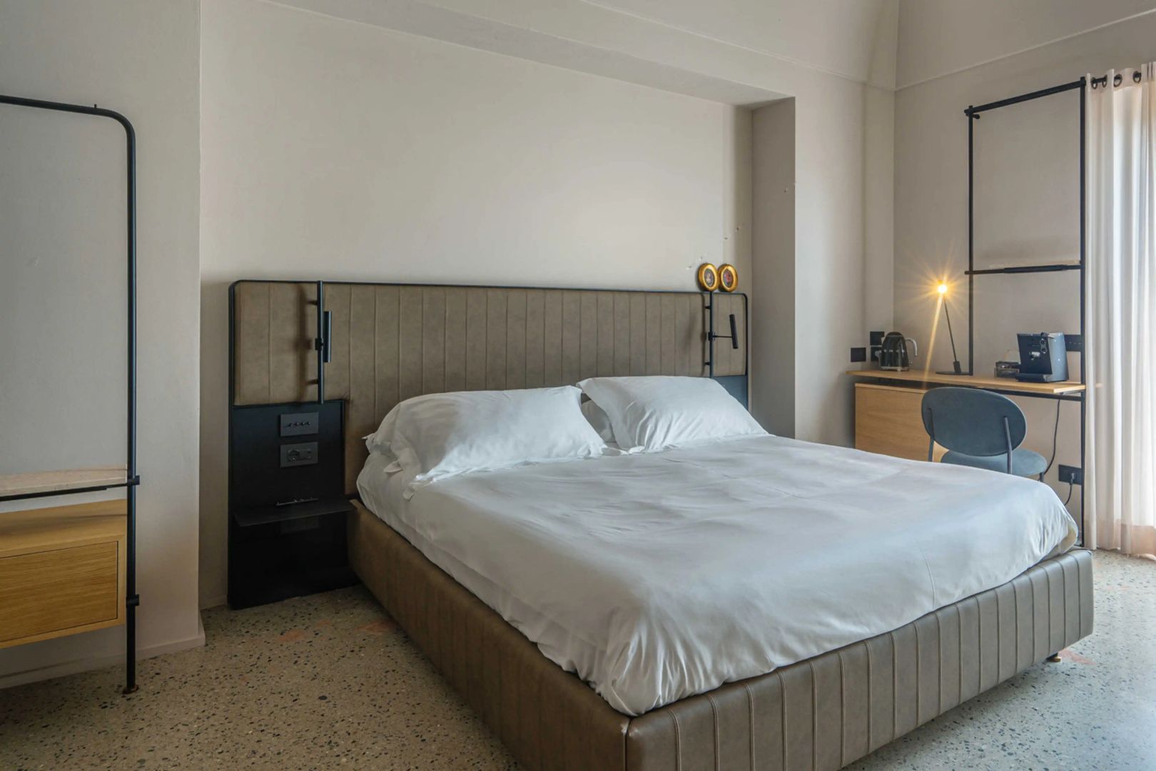 Doppelbett mit weißer Bettwäsche, gepolstertem Kopfteil und Nachttischlampen vor hellen Wänden.