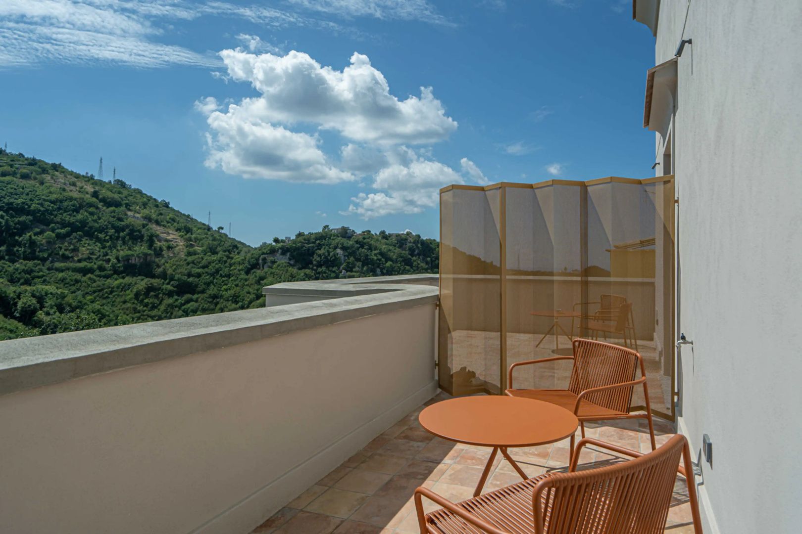 Terrasse mit orangen Stühlen und Ausblick auf bewaldete Hügel unter blauem Himmel.
