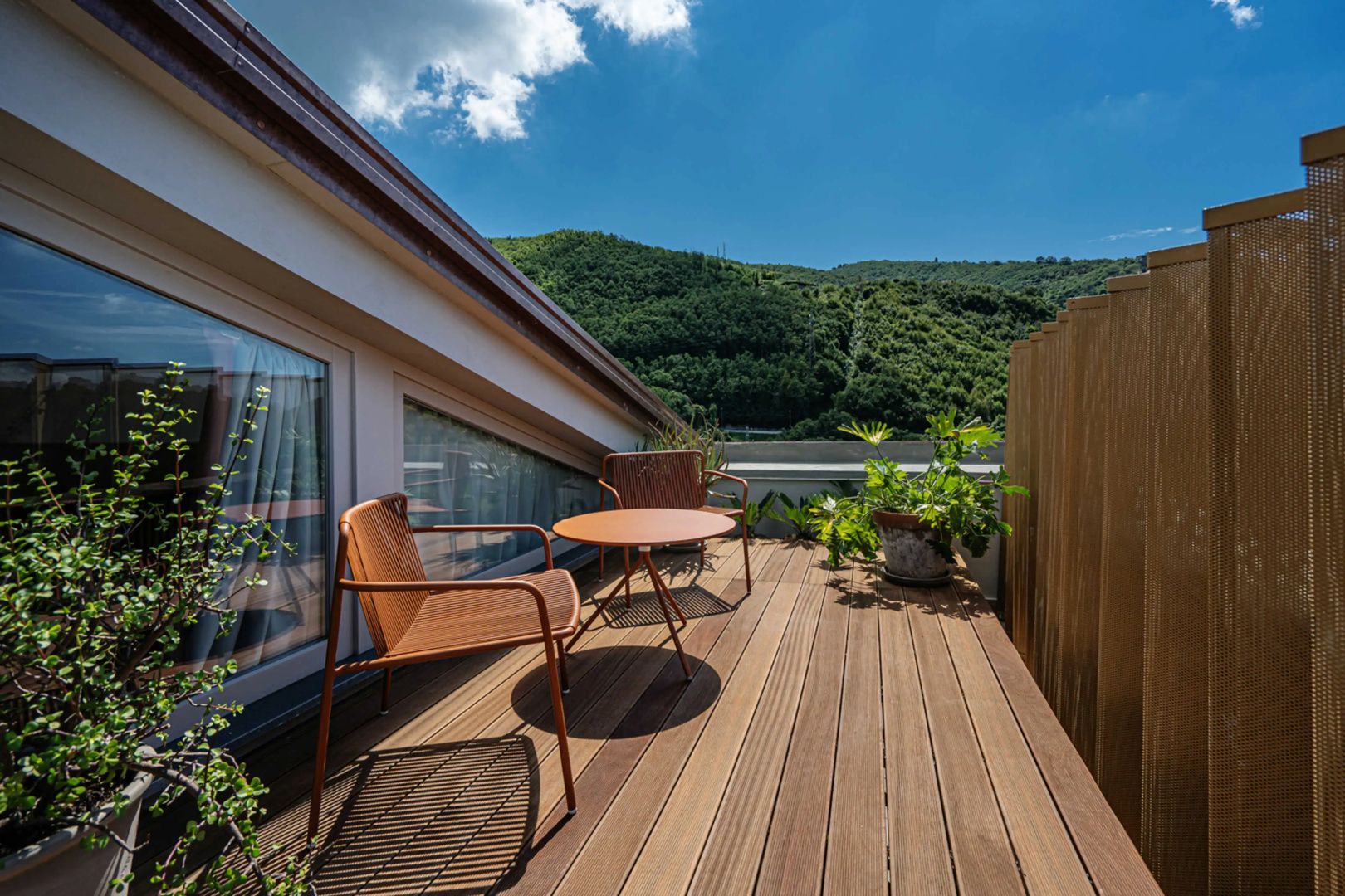 Holzterrasse mit orangen Balkonmöbeln und Blick auf grüne Berghänge.