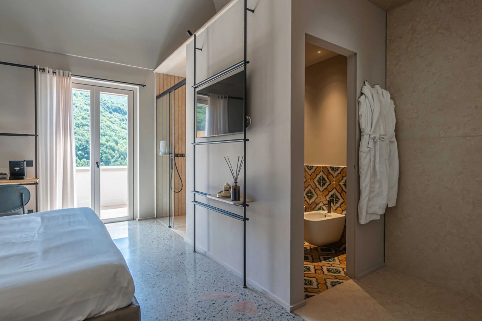 Modernes Hotelzimmer mit Balkontür, Fernseher an Metallgestell und Blick ins Badezimmer.