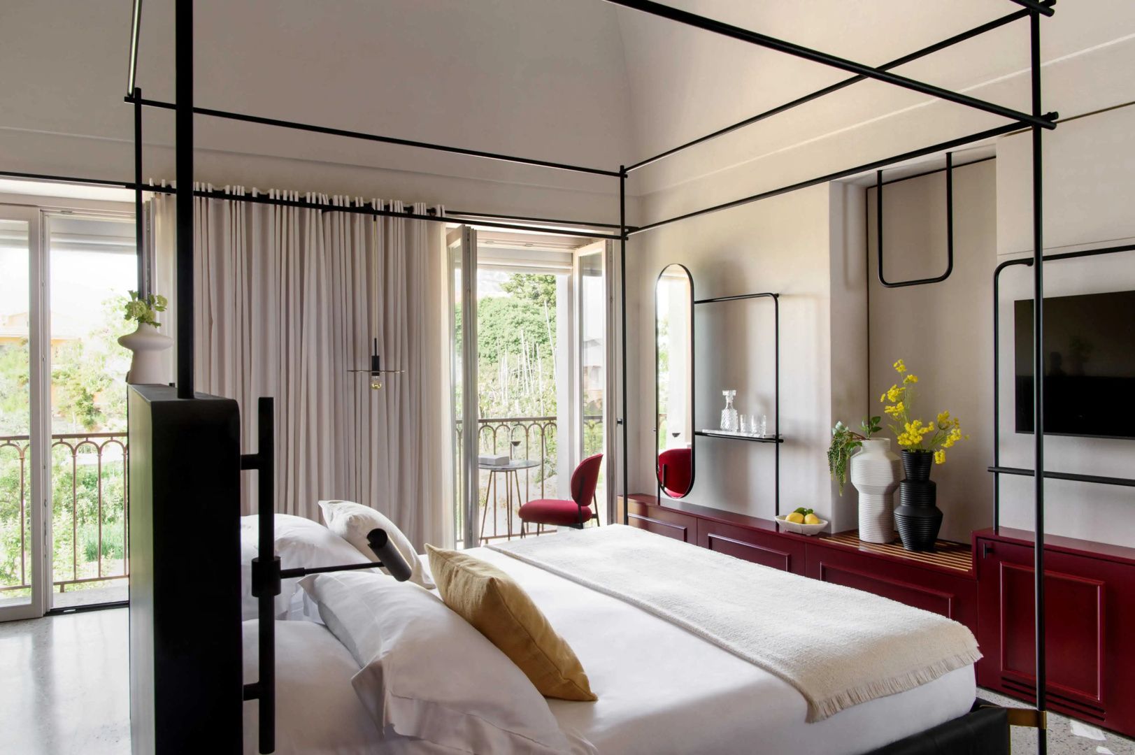 Helles Schlafzimmer mit Metall-Himmelbett, roten Wandmöbeln und Blick durch die Balkontür.