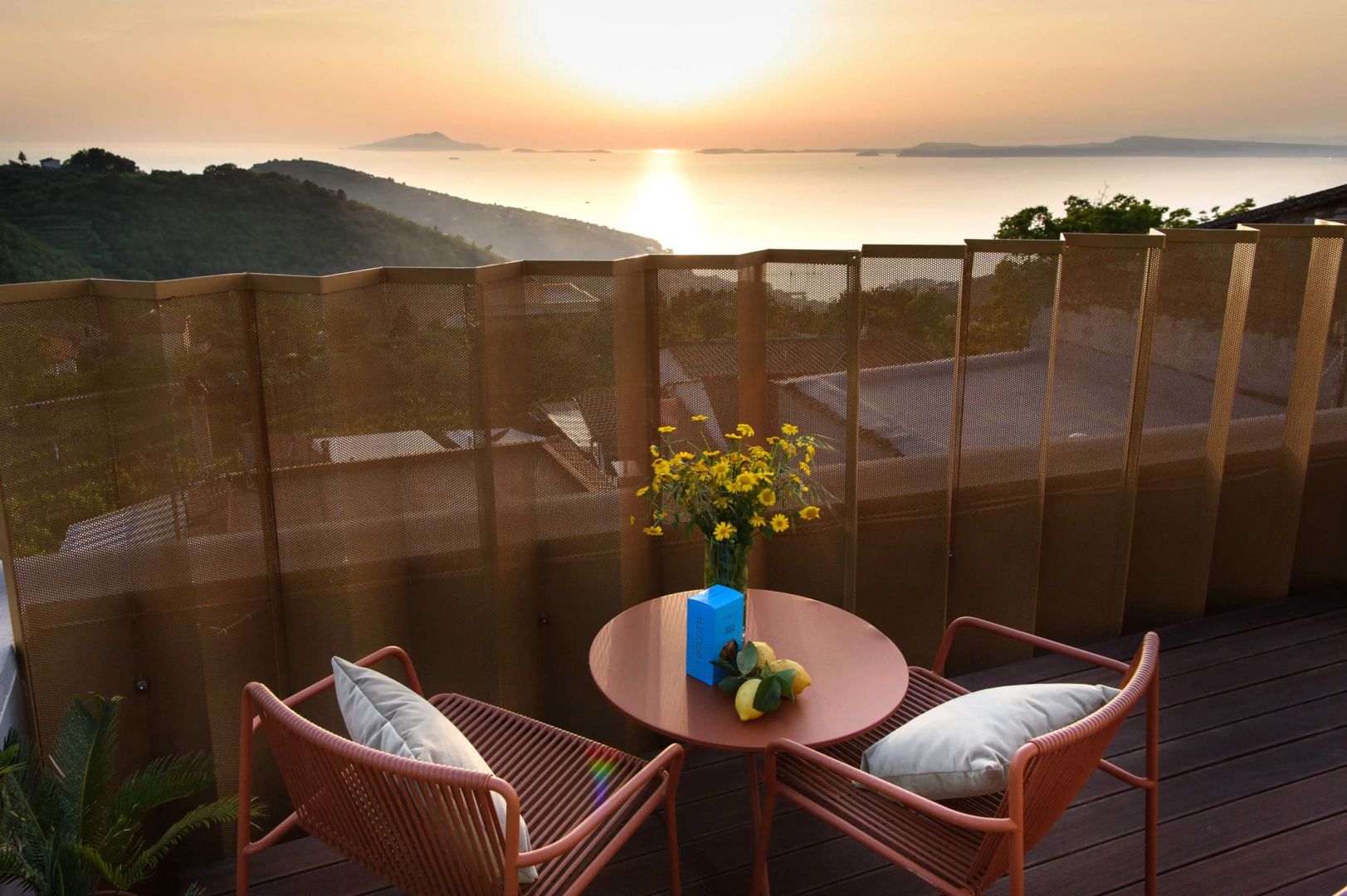 Terrasse mit roten Sesseln und Tisch mit Blick auf das Meer während des Sonnenuntergangs.