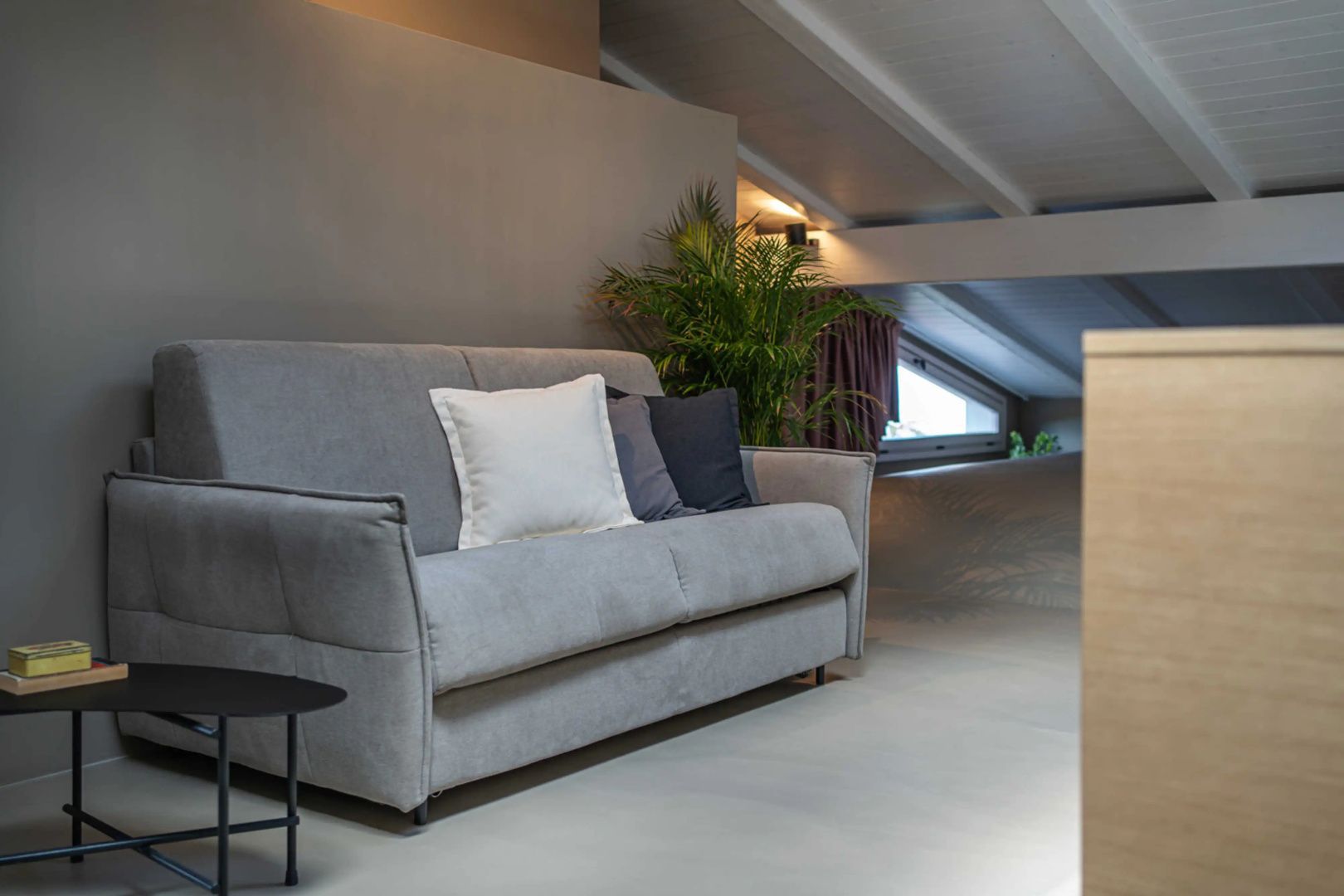 Graues Polstersofa mit Kissen in einem Zimmer mit Dachschräge und Pflanze.
