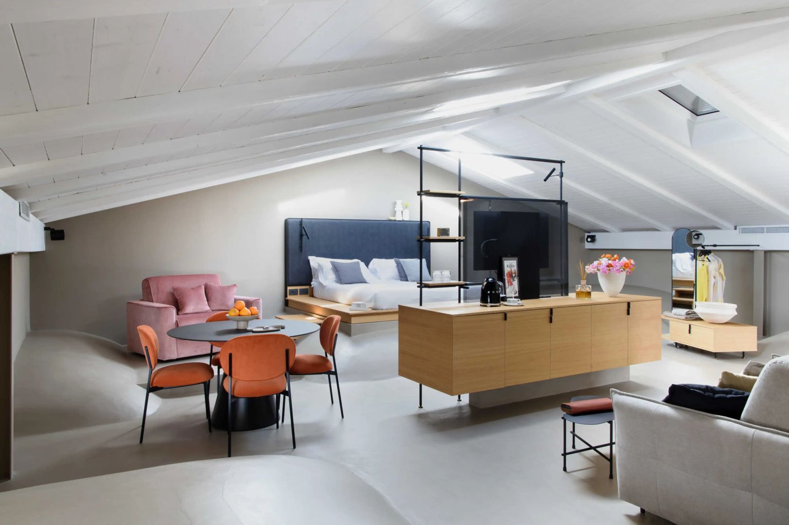 Dachgeschoss-Suite mit weißer Holzdecke, Podestbett und Essbereich mit orangefarbenen Stühlen.