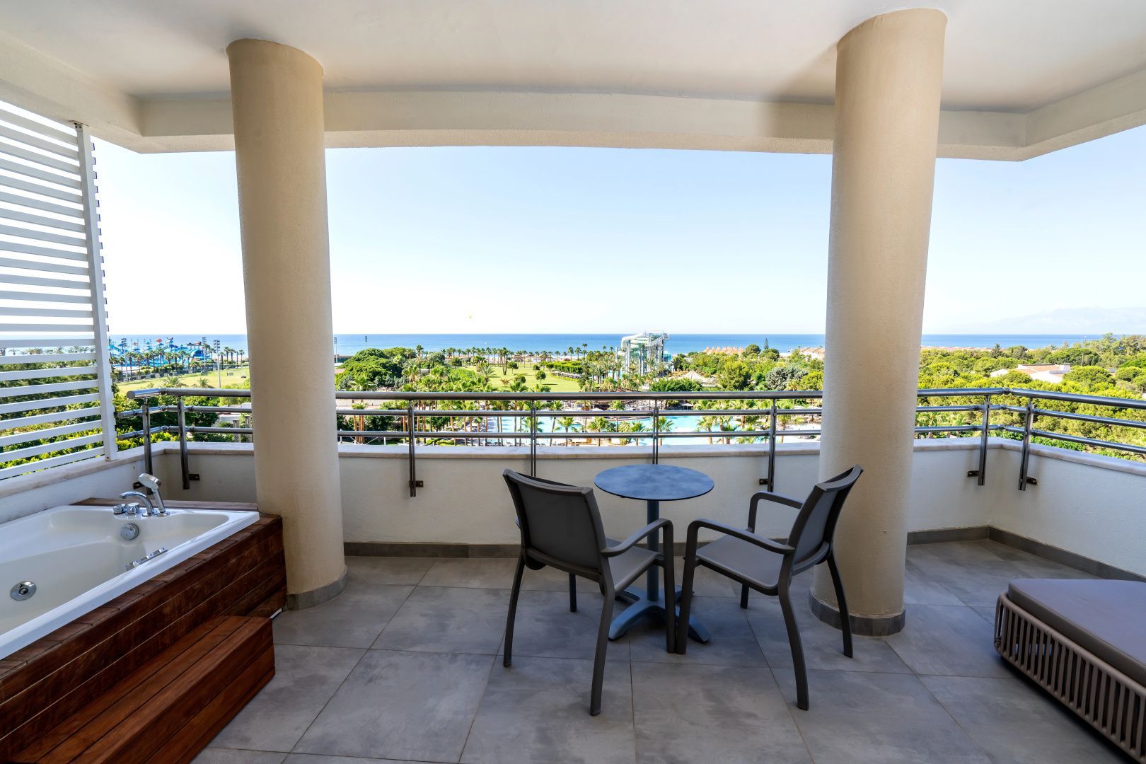 Blick vom überdachten Balkon mit Sitzgelegenheit auf die Hotelanlage und das Meer.