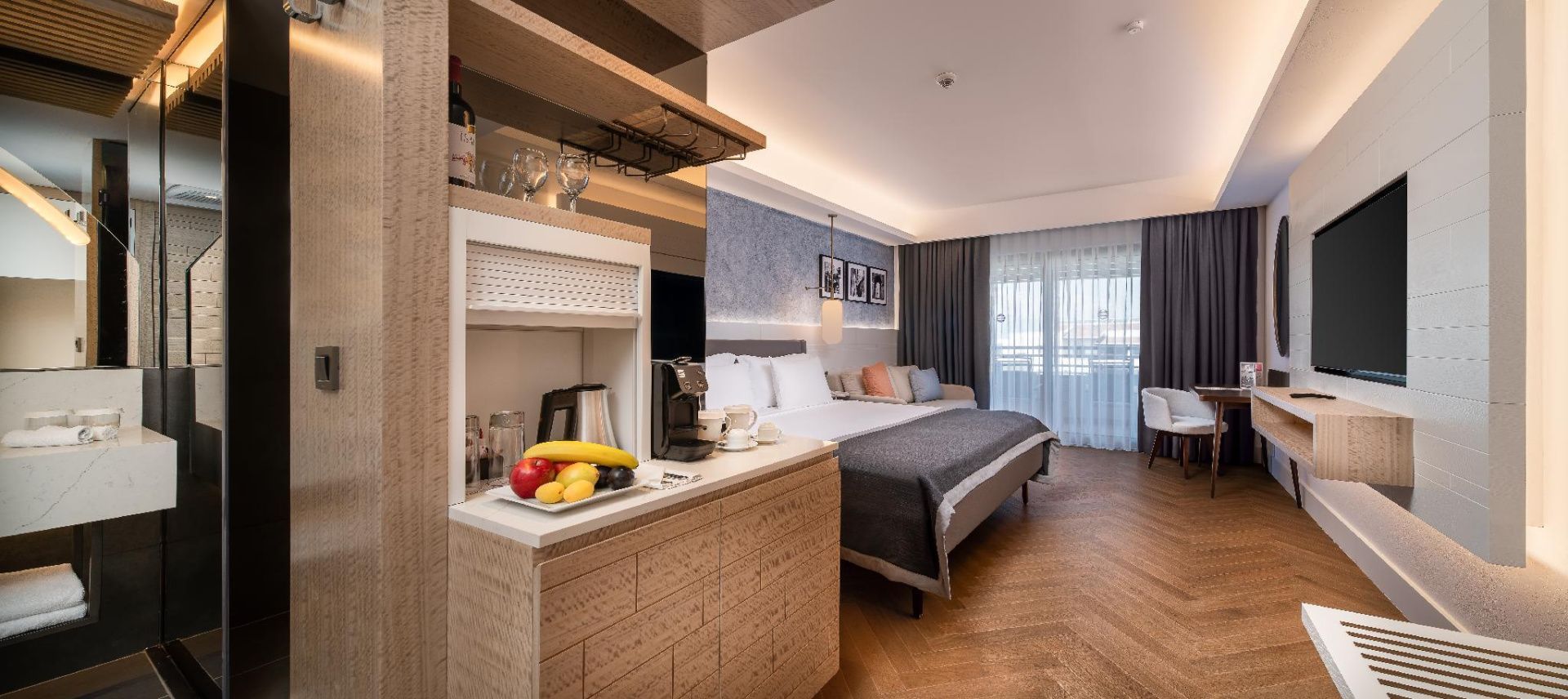 Modernes Hotelzimmer mit Doppelbett, Sitzbereich und Anrichte mit Obstschale.