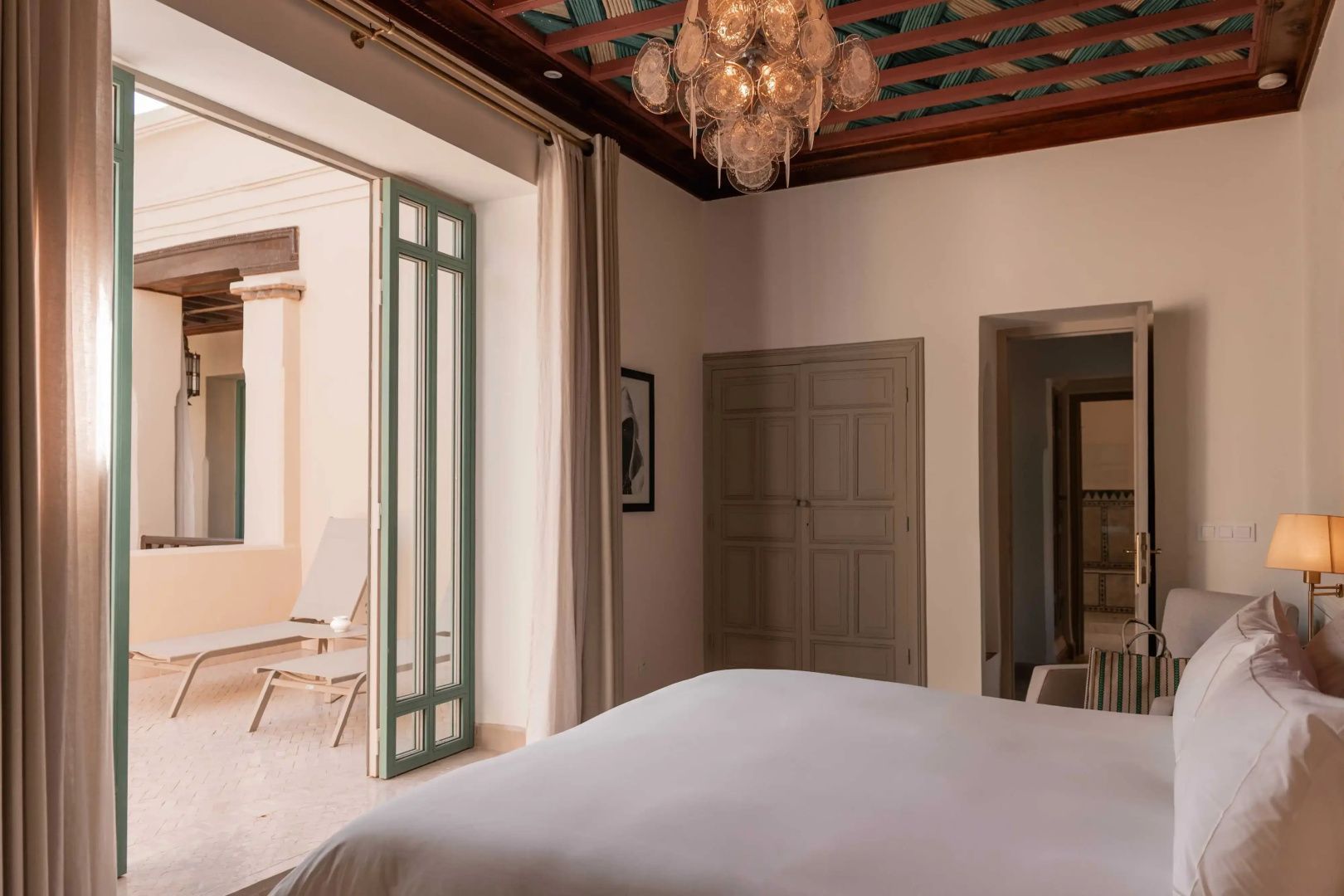 Blick in ein Hotelzimmer mit verzierter Decke, Kronleuchter und geöffneter Tür zur Terrasse.