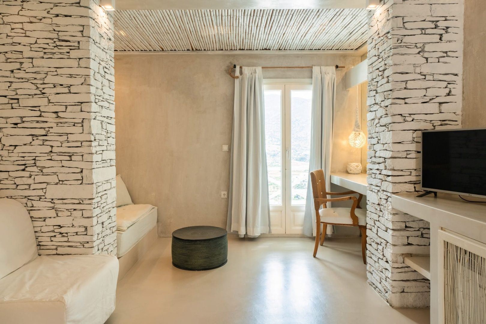 Wohnbereich einer Suite mit Naturstein-Elementen, Beistelltisch, Stuhl und hellen Vorhängen.