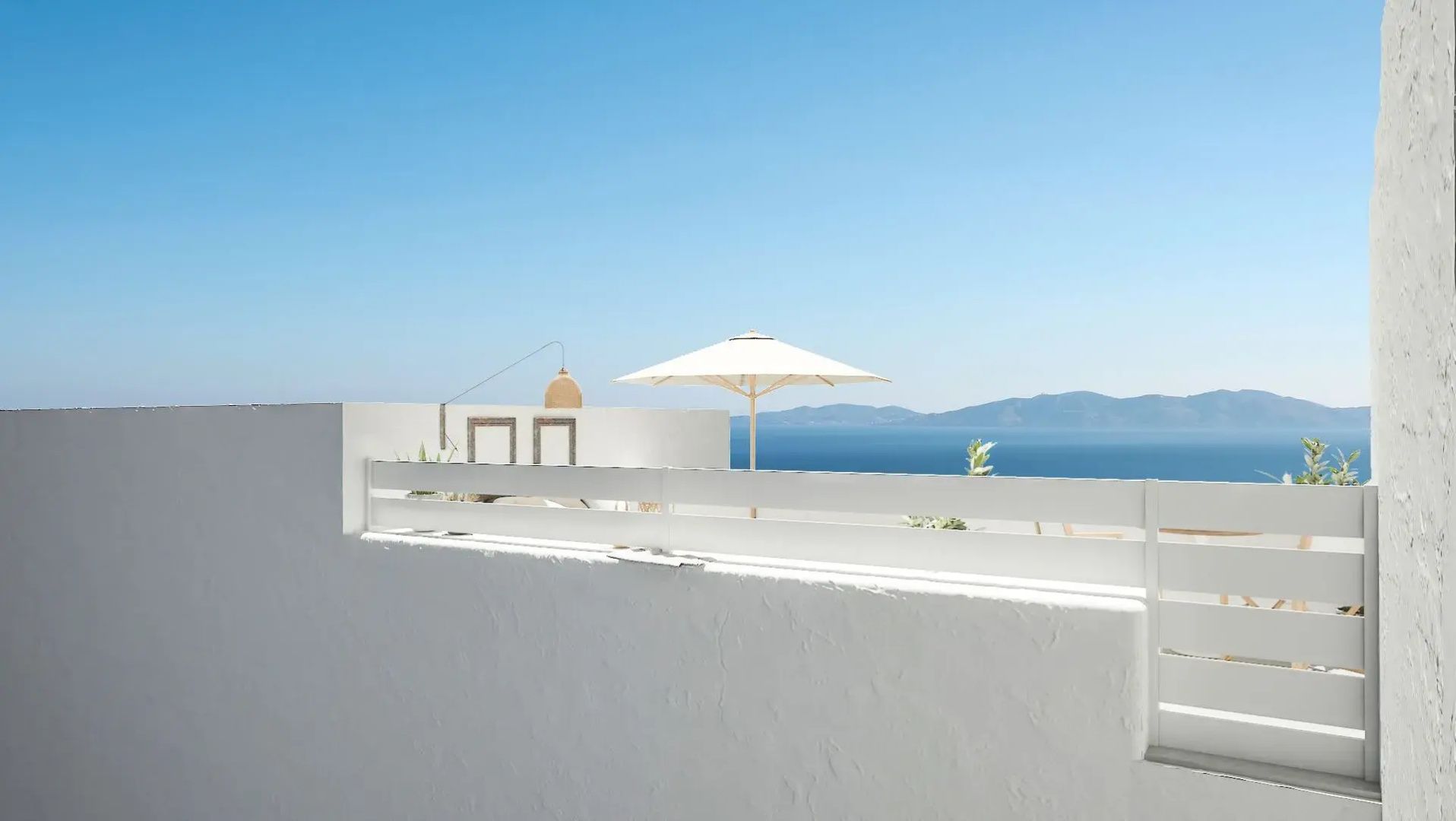 Terrassenmauer mit Sonnenschirm und Blick auf das blaue Meer sowie Berge am Horizont.
