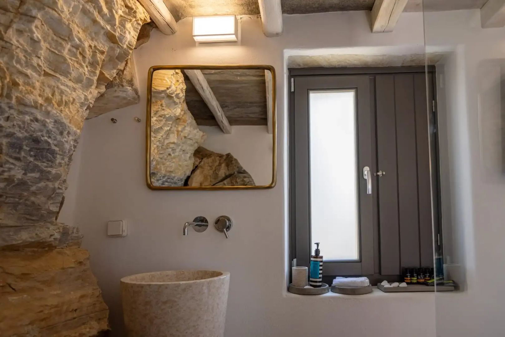 Waschbecken aus Stein und ein rechteckiger Spiegel an einer weißen Wand.