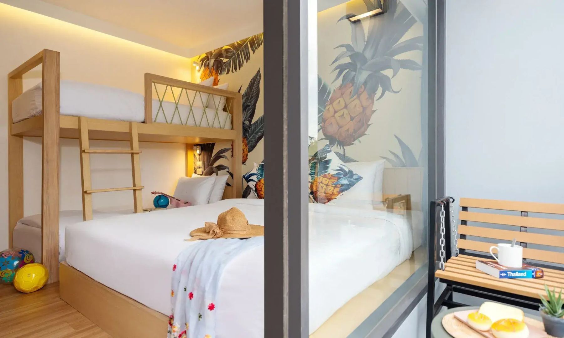 Blick durch ein Fenster auf ein Doppelbett mit Strohhut und ein Hochbett vor Tropentapete.