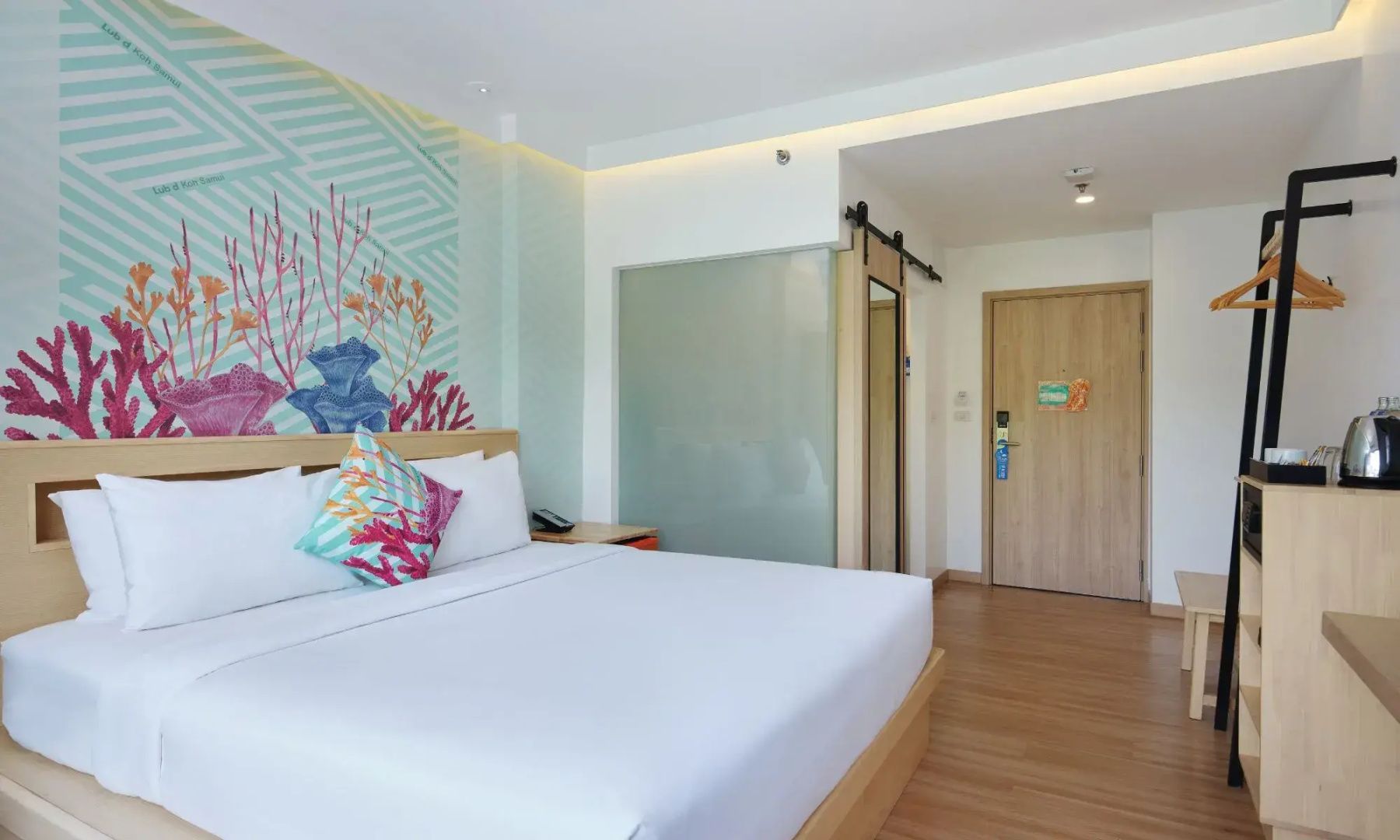 Doppelzimmer mit weißem Bett, buntem Wandmotiv und Vorraum mit Holztür.