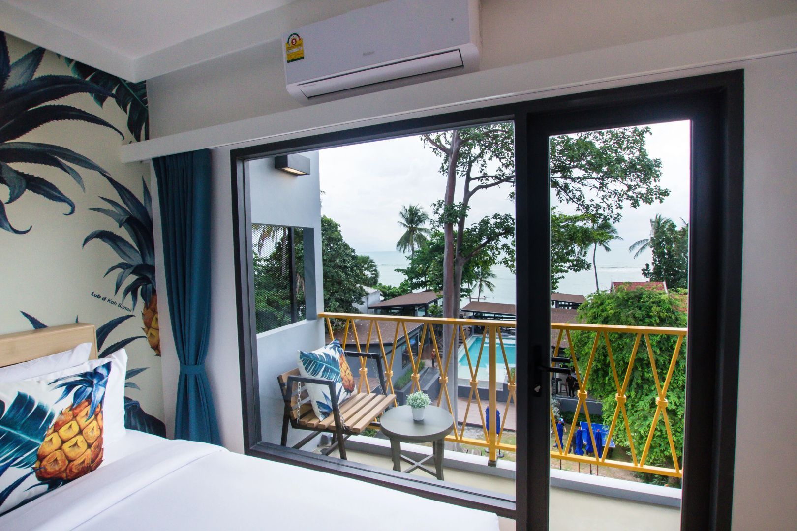 Blick vom Zimmer über den Balkon auf den Außenpool und die umliegenden Bäume.
