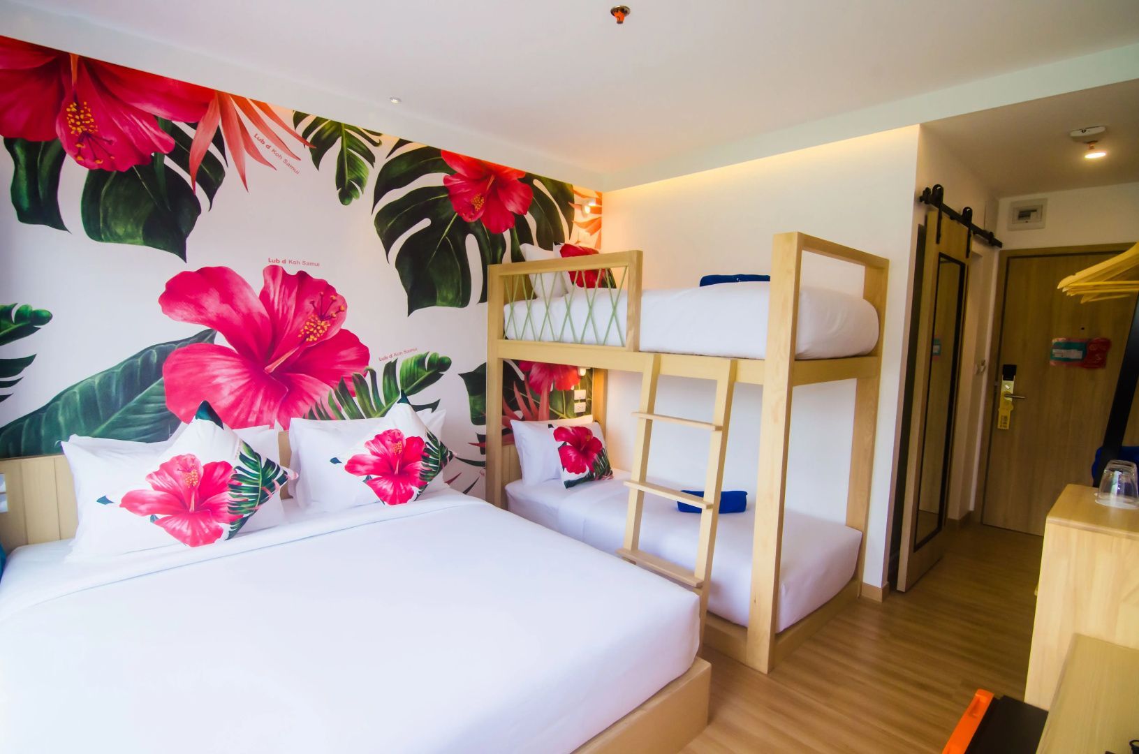 Familienzimmer mit großem Doppelbett, hölzernem Etagenbett und bunter Blumendekoration.