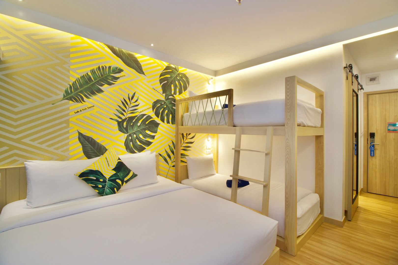 Hotelzimmer mit Doppelbett und hölzernem Etagenbett vor einer gelb grünen Mustertapete.