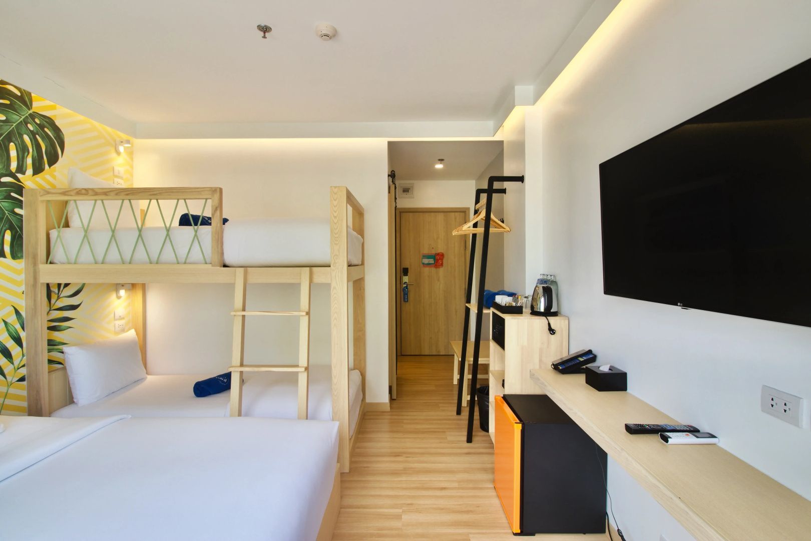 Blick in ein Hotelzimmer mit Etagenbett, Holzmöbeln, Fernseher und Flurbereich.