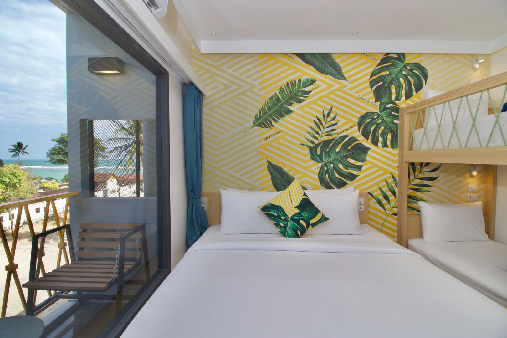 Schlafbereich mit weißem Doppelbett und großem Fenster mit Blick auf Balkon und Meer.