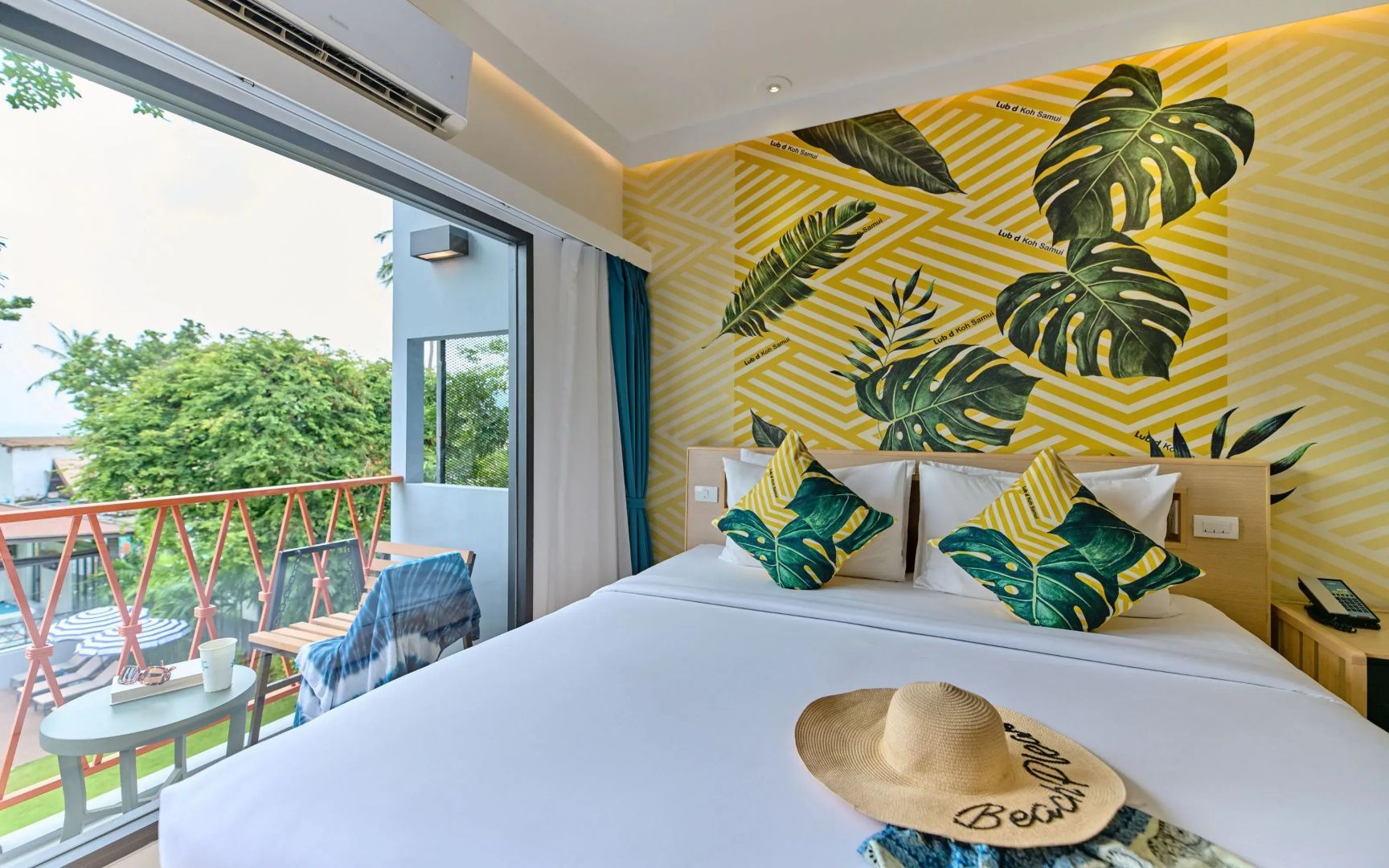 Doppelbett mit gelber Mustertapete, gemusterten Kissen und Blick zum Balkon.