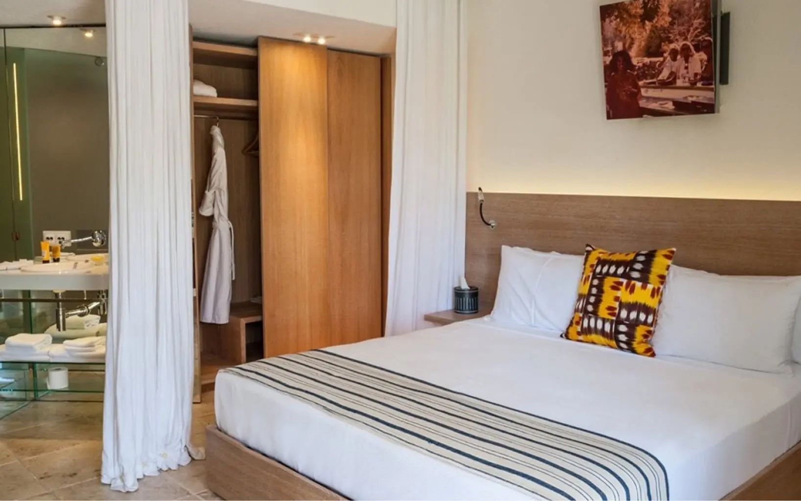 Hotelzimmer mit Doppelbett, hellem Holzschrank, weißem Bademantel und Vorhang.